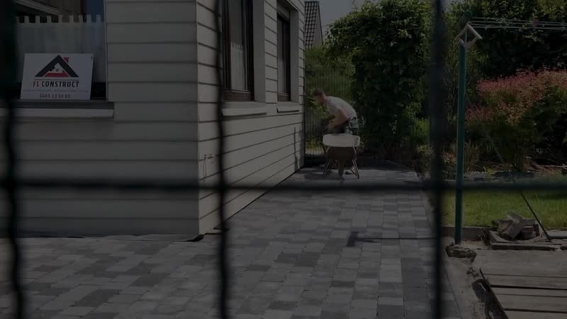 Allée en pavés en cours de pose devant une maison, panneau FL Construct à la fenêtre